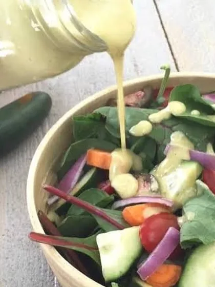 My Jalapeño Honey Mustard dressing being poured over a garden salad. It adds a creamy texture with a sweet and spicy kick.