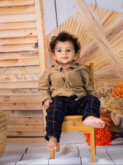 A classic seated portrait of a toddler on a small wooden chair, looking calm and composed.