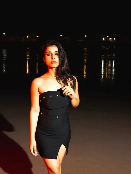A night beach shoot using flash to illuminate the model against the dark sea. The distant city lights add a beautiful bokeh effect.