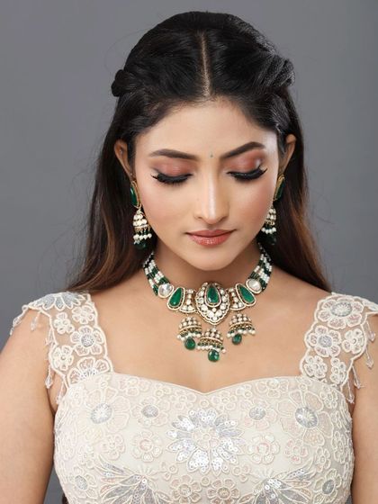A fresh and pretty look in a white lehenga with green jewelry. The makeup is soft and natural, with a focus on enhancing her beautiful smile.