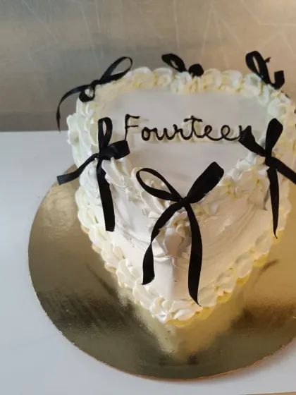 A chic and trendy heart-shaped cake for a fourteenth birthday. The minimalist design with black ribbons is a modern take on the classic celebration cake.