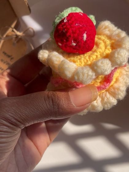 A hand holding the mini crochet cake to show its small, adorable size. It's a perfect little keepsake.