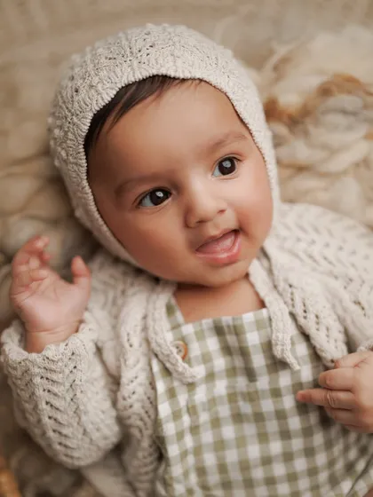 A sweet expression from a baby boy in a cozy knit bonnet and cardigan. Milestone sessions are full of these heart-melting moments that are a joy to capture.