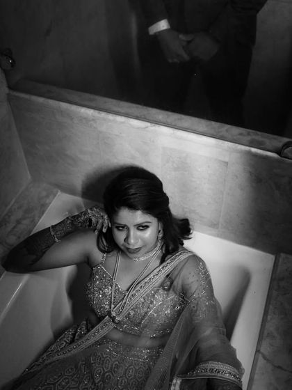 A creative black and white photo of the bride in her Sangeet outfit, posing in a bathtub for an artistic and unconventional portrait.