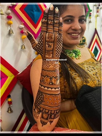 A smiling bride proudly displaying her intricate bridal mehendi. The design features personalized initials and traditional motifs, looking beautiful against her festive attire.