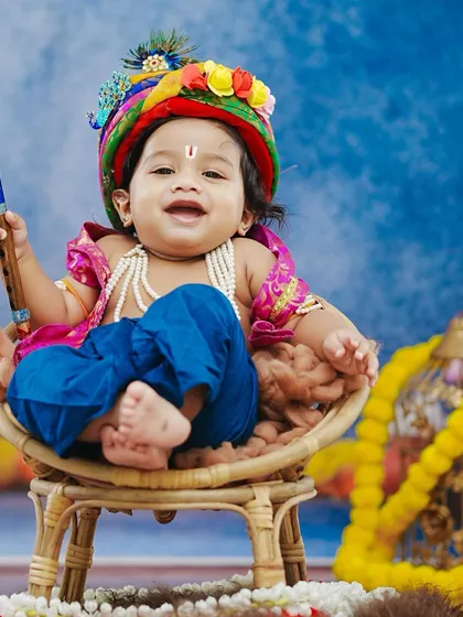 A joyful Bal Gopal, dressed in vibrant attire with a peacock feather in his turban, smiles happily for his Janmashtami portrait.
