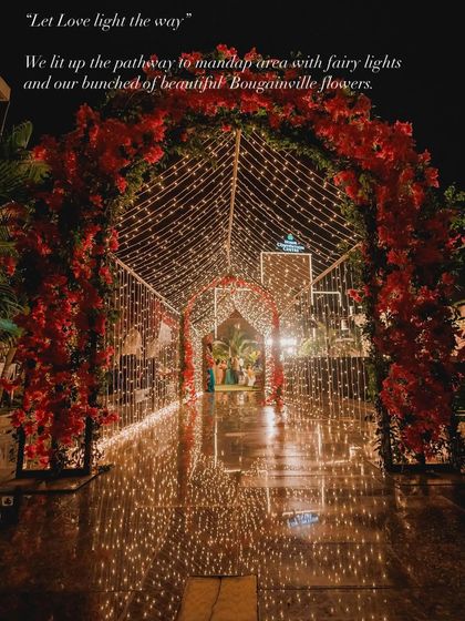 Let love light the way. For this wedding, we created an enchanting pathway to the mandap area with a tunnel of fairy lights, framed by arches of vibrant red bougainvillea flowers.