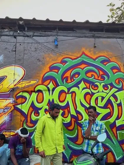Local residents sit and chat in front of a vibrant wall of graffiti at Sassoon Dock. This image shows how street art becomes a part of the everyday landscape and a backdrop for community life.