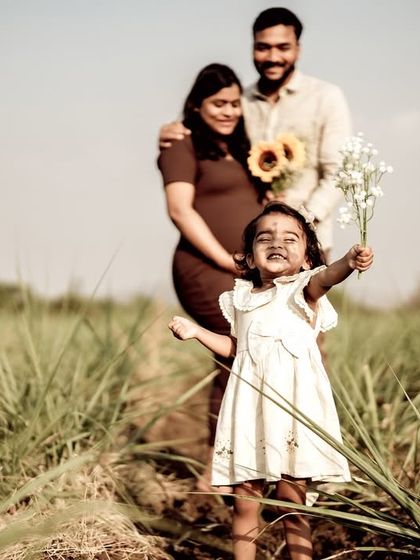 A joyful shot of the daughter in the foreground, holding up flowers with a big smile, while her parents stand lovingly in the background. It perfectly captures her excitement.