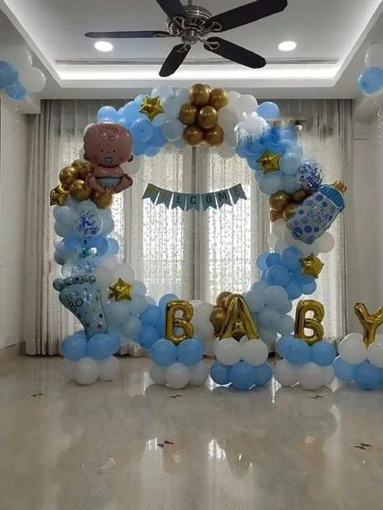 This baby shower or welcome home setup features a full ring of balloons in blue, white, and gold. The design includes "BABY" letter balloons, a banner, and themed foil balloons like a baby bottle and character.