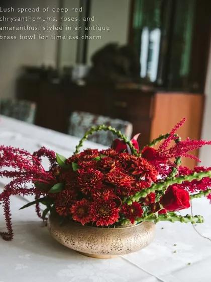 We believe luxury is found in the details. This centerpiece features a lush arrangement of deep red chrysanthemums, roses, and amaranthus in an antique brass bowl, adding a touch of timeless charm and elegance to the tablescape.
