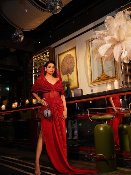 The full silhouette of the crimson red slit gown, complete with its structured hood and dramatic train. A look designed for power and poise.