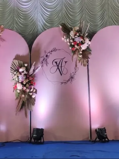 A sophisticated and trendy engagement stage with a modern boho-chic theme. The backdrop consists of three soft pink arched panels, personalized with the couple's initials and adorned with elegant arrangements of pampas grass and flowers.