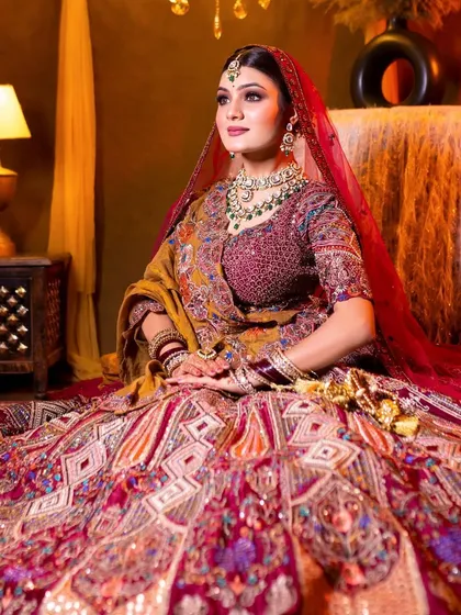 A full shot of a bride seated, showcasing her entire look. The green Kundan jewellery provides a beautiful contrast to her deep red and yellow lehenga.