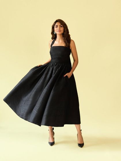 A full-length shot that captures the classic, Audrey Hepburn-esque elegance of this black halter dress.