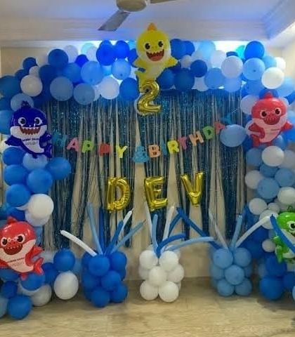 A Baby Shark themed 2nd birthday party with a blue balloon arch, character foil balloons, and a shimmering backdrop.