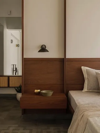 In this bedroom from Apartment 1005, a custom wood-paneled headboard extends across the wall, integrating the nightstand. A large mirror reflects the space, enhancing the room's depth and showcasing the thoughtful, built-in design.