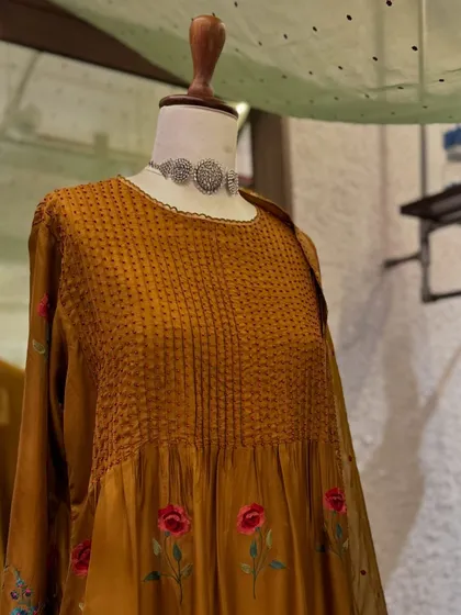 A close-up of the mustard kurta, showing the textured pintuck bodice and the delicate floral embroidery along the hem.