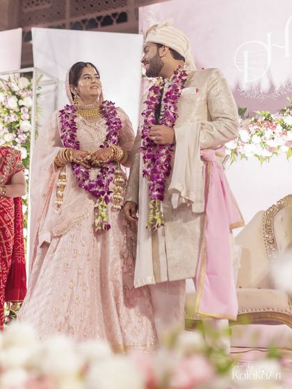 A full-length shot of the couple after the varmala ceremony, showcasing their beautiful coordinated outfits and the overall aesthetic of the stage.