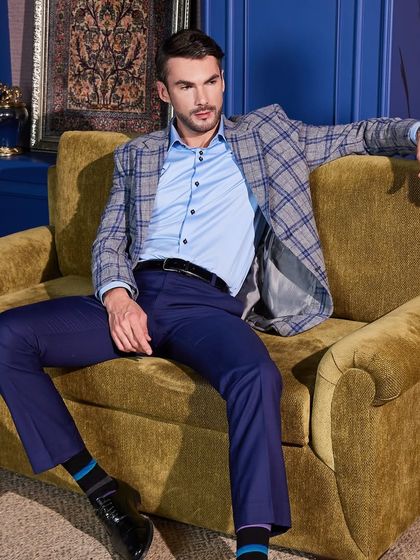 A grey and blue plaid sports jacket paired with navy trousers creates a sophisticated, smart-casual look. This is custom tailoring that feels relaxed but looks sharp, perfect for a business lunch or creative workplace.