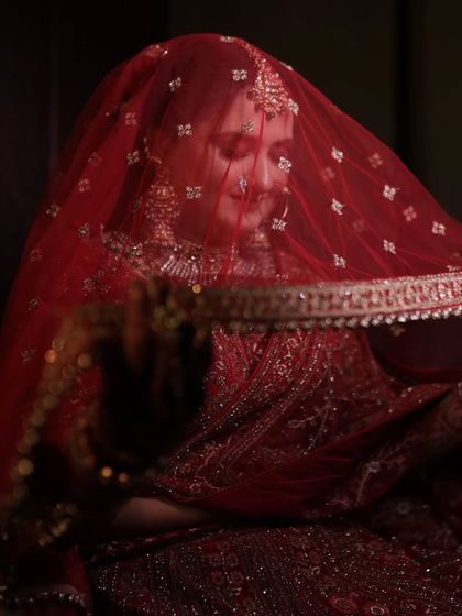 Another beautiful shot of the bride under her veil. This angle captures her adjusting the dupatta, adding a sense of movement and candidness to this traditional bridal portrait.