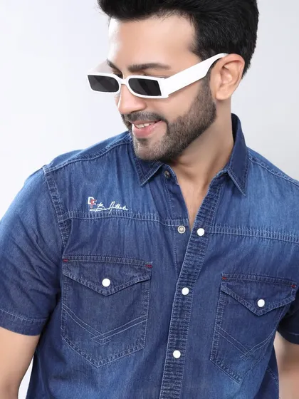 A model pairs a denim shirt with trendy white sunglasses. This shot has a cool, modern feel, perfect for a youthful fashion brand's online store.