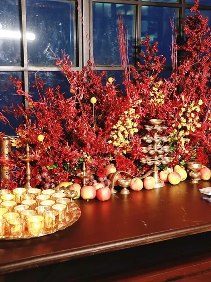 A festive tablescape with candles, fruit, and beautiful red and yellow floral arrangements.