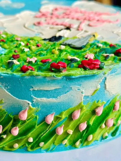 A close-up detail of the palette knife work on the side of the countryside cake, showing the texture of the grass and tiny pink flowers.