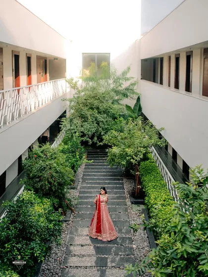 A high-angle shot of the bride standing in a modern courtyard, the symmetry of the architecture and lush greenery creating a beautiful frame.