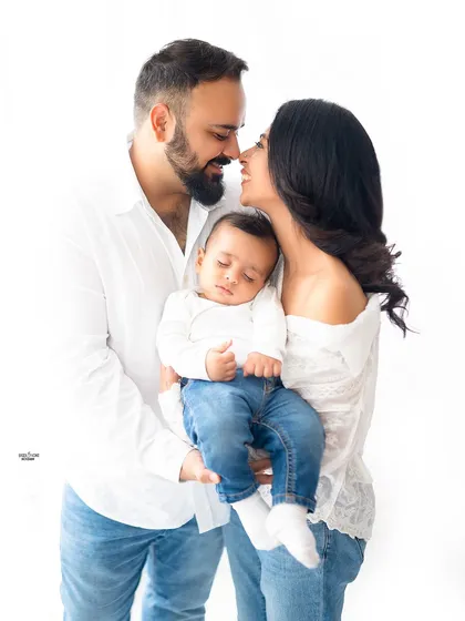 A sweet family moment, with the parents about to share a kiss over their sleeping baby.