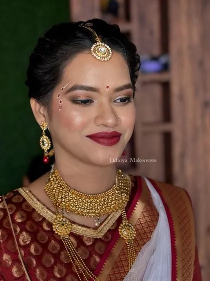 A soft glam beauty look for a wedding guest. This look features a classic red lip and subtle, traditional face painting (Kolka design) for an elegant touch.