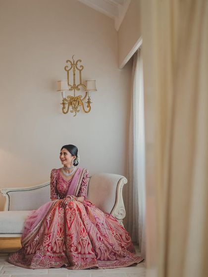 This wider shot captures the grandeur of the bride's attire and the serene setting. Her makeup remains a focal point, glowing softly even from a distance.