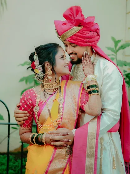 A tender embrace between a bride and groom in their stunning Maharashtrian wedding attire. The bride's yellow and pink saree complements the groom's traditional outfit perfectly.