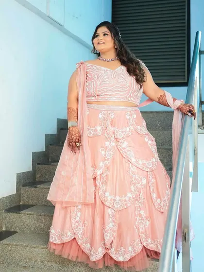 The bride posing on the stairs, showcasing the beautiful silhouette and drape of her engagement lehenga.