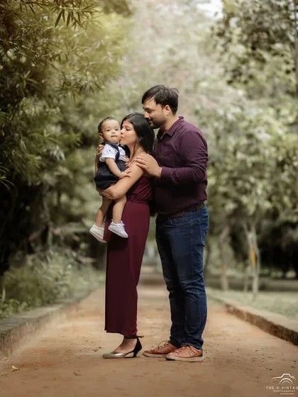 A classic family walking portrait in a beautiful park. The mother's gentle kiss on her son's cheek is a perfect, candid moment.