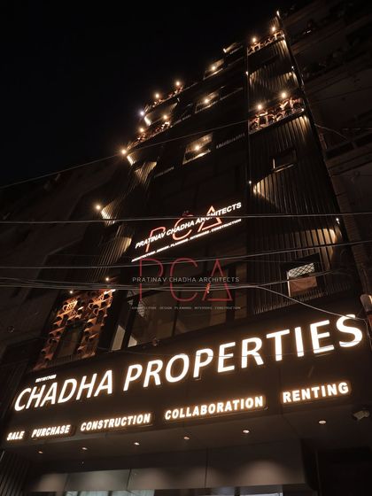 The illuminated signage and facade of the Chadha Properties office at night. The lighting design ensures the building is a landmark on the street, clearly communicating the business's services.