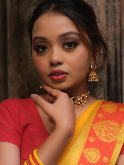 A classic portrait featuring a soft brown smoky eye and a warm red lip. This timeless combination is perfect for any festive occasion and complements the yellow and red saree beautifully.