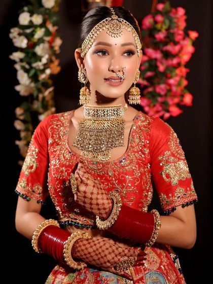 A full-length view of a bride in a striking red lehenga. The makeup is balanced to complement the heavy embroidery and jewelry, ensuring a cohesive and stunning overall look.
