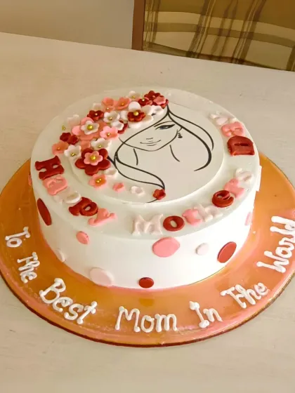 An elegant Mother's Day cake with a line-art illustration of a mother, adorned with small sugar flowers. The message reads "To the Best Mom in the World."
