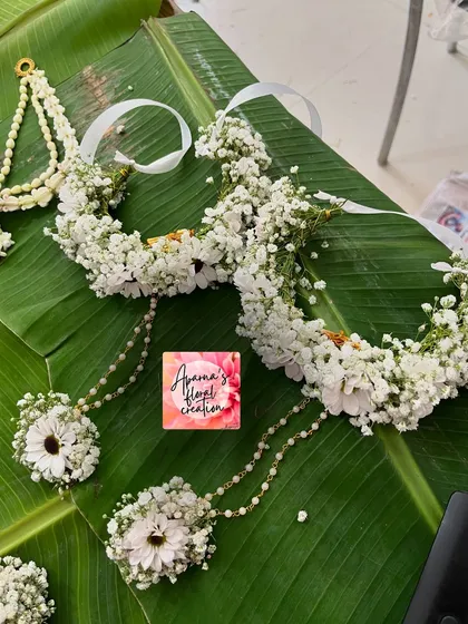 A partial view of an all-white Haldi set, featuring a floral crown and hath phool made with daisies and baby's breath.