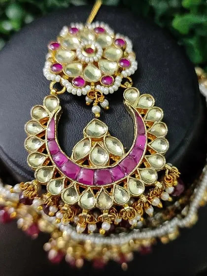 The maang tikka from this set, featuring a crescent shape with vibrant pink accents.