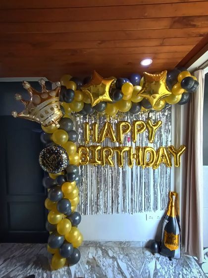A black and gold themed birthday party with a balloon arch, foil letters, and props like a crown and champagne bottle.