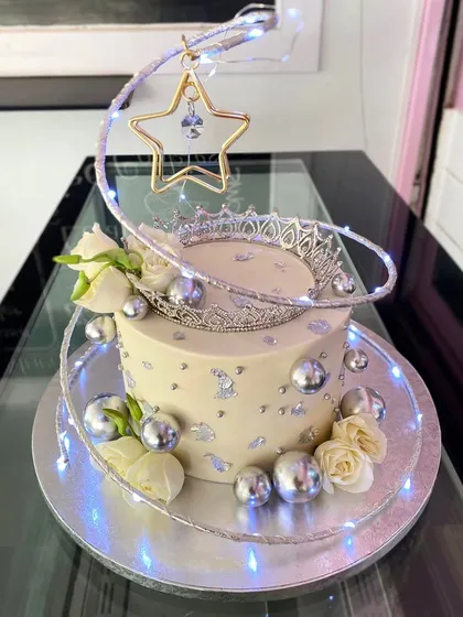 A glamorous anniversary cake with a silver crown, silver spheres, and twinkling fairy lights.