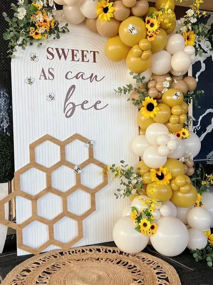A "Sweet as can Bee" themed baby shower. This creative setup features a honeycomb cutout, a custom backdrop, and a beautiful balloon garland with sunflowers.
