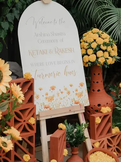 Welcome to the Haldi! We styled this entrance with rustic terracotta pots, cheerful sunflowers, and a custom welcome sign to set a warm and inviting tone for the "turmeric hues" celebration.