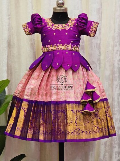 A rich purple and pink Kanchi Pattu lehenga. The blouse has a petal-style peplum, and the skirt features a wide, shimmering gold border.