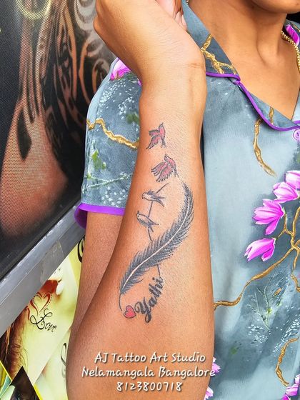 A feather tattoo that transforms into birds, with a name incorporated into the design.