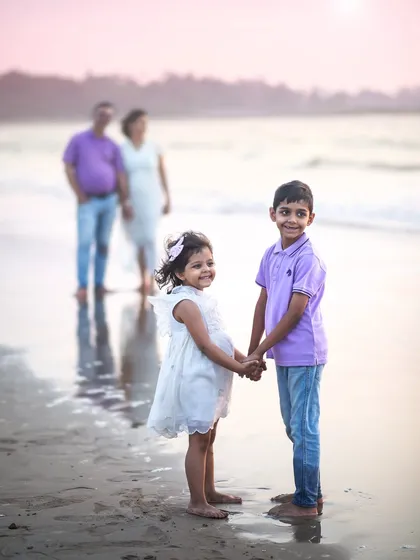 A sweet sibling portrait on the beach, with their parents watching lovingly in the background. This composition tells a beautiful story of family.