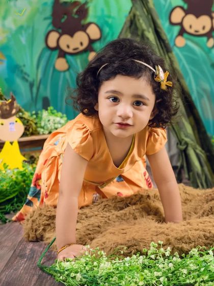 A close-up shot of a toddler crawling through the jungle props, looking directly at the camera with her big, curious eyes.