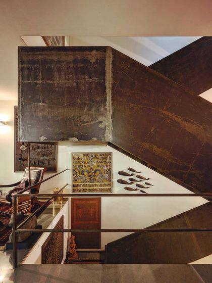 A staircase crafted from folded, patinated metal plates becomes a dominant sculptural feature in this interior. The raw, textured materiality of the steel provides a strong contrast to the smooth white walls.